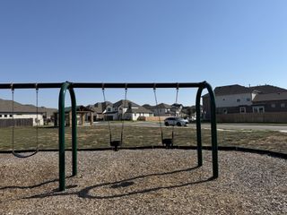 Community Amenities A green metal swing set in a community park, offering fun for kids in Blackhawk by GFO Home (Pflugerville, TX).