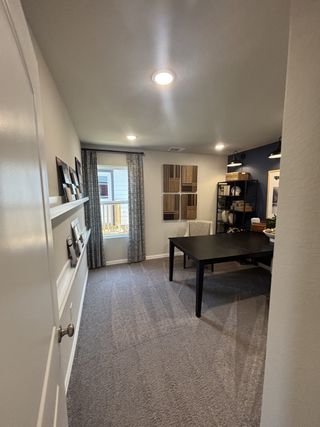 A stylish office space with carpet, wall-mounted decor, and ample lighting in Red Hawk Landing by HistoryMaker Homes (San Antonio, TX).