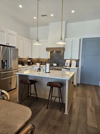 A modern kitchen with a marble island, sleek cabinetry, pendant lighting, and hardwood floors.