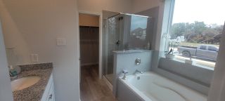 A modern bathroom with a glass-enclosed shower, granite vanity, and a large window above the bathtub.