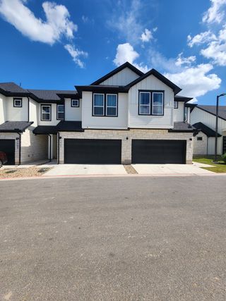 Street view Modern two-story townhome with stone façade and dark shutters in Townhomes at Gattis by Green Abode Developers (Round Rock, TX).