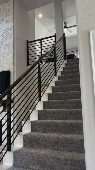 A modern staircase with plush carpeting, sleek metal railing, and a textured stone accent wall, leading to an upper level.