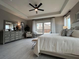 Stunning master bedroom with large windows, white and neutral decor, a ceiling fan, and modern furnishings.