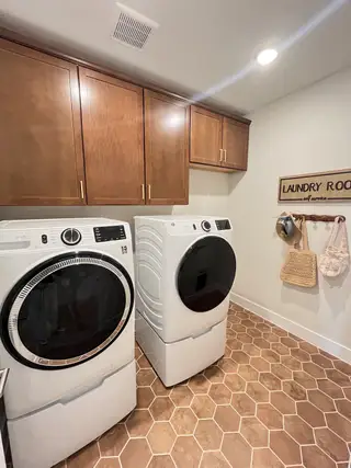 A modern laundry room with sleek appliances, wooden cabinets, and hexagonal floor tiles.