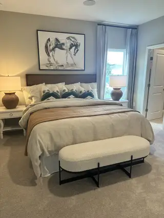 Model Home A cozy bedroom with elegant bedding, tasteful artwork, and natural light filtering through large windows.