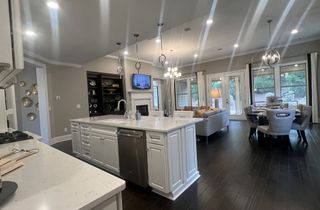 Model Home An elegant open-concept kitchen with a large island, dark hardwood floors, and modern lighting, leading to a cozy living area.