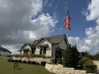 Model Home A stunning stone-accented home with a manicured lawn and American flag in Double Eagle Ranch by Double Eagle Ranch (Cedar Creek, TX).