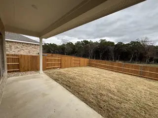 A covered patio looking out onto a fenced backyard with a view of trees and grassy lawn.