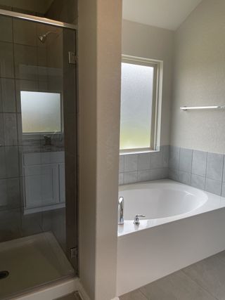 A modern bathroom with a sleek glass shower, spacious soaking tub, and frosted window for privacy.