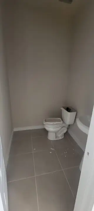 A minimal bathroom with beige walls, tiled floor, and a simple white toilet and sink setup.
