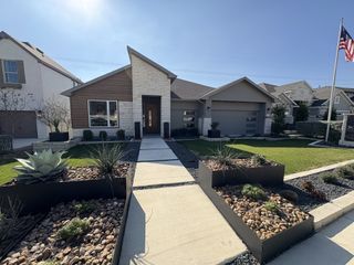 A stylish modern home with a stone and stucco facade, angular rooflines, and a bright orange front door in Esperanza by Scott Felder Homes (Boerne, TX).
