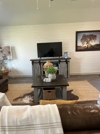 A cozy living room with a shiplap wall, TV console, rustic coffee table, and leather sofas. Warm and inviting decor.