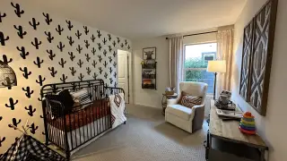 A cozy nursery with a cactus accent wall, modern black crib, soft lighting, and comfortable seating.