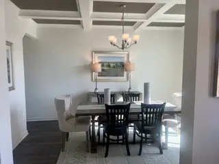 Model Home A chic dining room features a coffered ceiling, elegant chandelier, and stylish seating arrangement with neutral decor.
