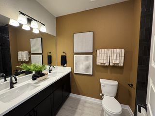 Model Home A modern bathroom featuring dual sinks, bold lighting, and decorative wall art.