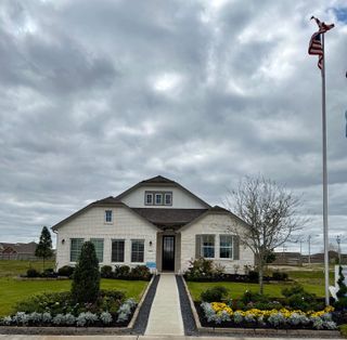A charming single-story white brick home with a landscaped yard in The Commons at Sedona by K. Hovnanian® Homes (League City, TX) under a cloudy sky.