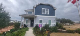Street view A charming blue and gray two-story home with lush landscaping in Timber Creek by Legend Homes (San Antonio, TX).