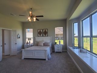 A spacious bedroom with large windows, carpeted flooring, and a cozy white bed set alongside elegant décor.