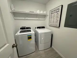 A modern laundry room with a sleek washer and dryer, open shelving, and wood-look flooring.