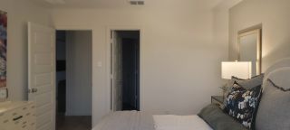 Model Home A cozy bedroom featuring neutral walls, a stylish bedside lamp, and a floral accent pillow on the bed.