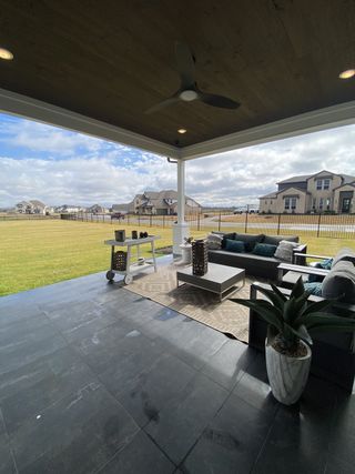 A cozy covered patio with modern seating, stylish fan, and expansive views of a lush yard, perfect for relaxation.