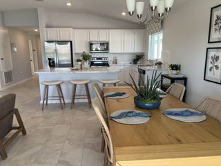 Model Home A modern kitchen and dining area with white cabinets, light tile flooring, and a wooden table adorned with plants.