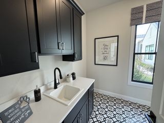 Model Home A modern laundry room featuring black cabinets, a sleek faucet, geometric floor tiles, and a bright window.