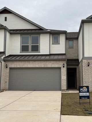 A contemporary townhome with a gray garage door, brick detailing, and clean lines in Whitestone Preserve by Pulte Homes (Cedar Park, TX).