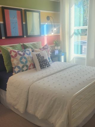A vibrant bedroom with colorful striped walls, eclectic art, and cozy bedding, featuring playful pillows and ample natural light.