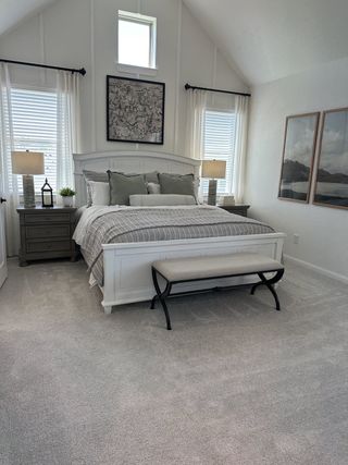 Model Home A cozy bedroom with vaulted ceiling, elegant decor, soft gray carpeting, and a serene color palette.