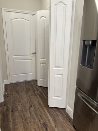 A modern kitchen pantry with warm wood floors, white paneled doors, and a sleek stainless steel refrigerator.