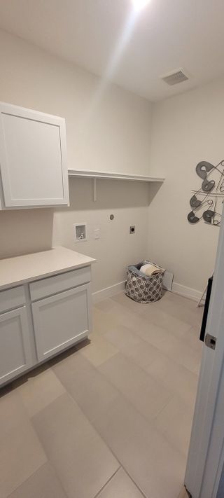 Model Home A bright laundry room with sleek white cabinets, ample shelving, and neutral tile flooring.