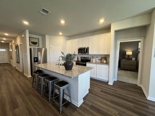 Modern kitchen with white cabinetry, granite countertops, stainless steel appliances, and sleek bar seating on wood flooring.