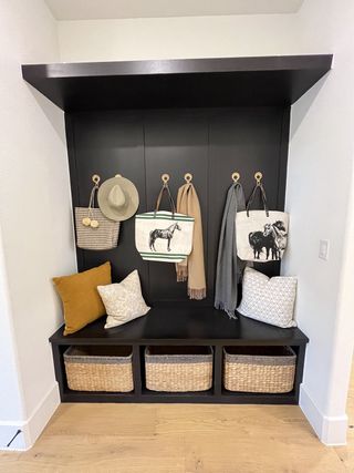 A cozy mudroom nook with a sleek black bench, woven baskets, and chic hanging hooks for bags and hats.