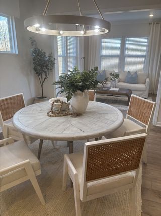 Model Home A cozy dining area with a round wooden table, wicker-backed chairs, modern lighting, and a view of the inviting living room.