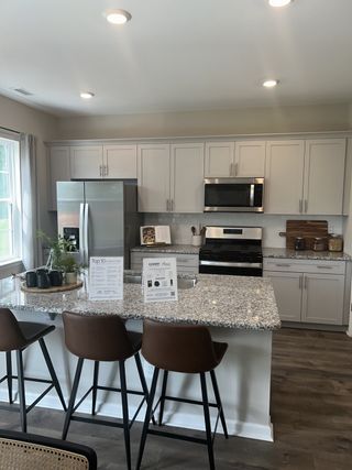 Model Home A modern kitchen with granite countertops, stainless steel appliances, sleek cabinetry, and stylish bar seating.