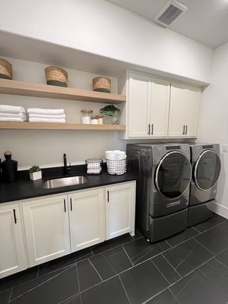 Model Home A sleek laundry room featuring modern appliances, black countertops, and open shelving for stylish, practical storage.