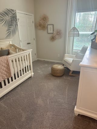 A cozy nursery with soft carpeting, a white crib, a comfy chair, and charming wall decor featuring floral accents.