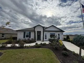 Model Home A charming white brick home with black shutters and a manicured front yard in Carillon by D.R. Horton (Manor, TX).