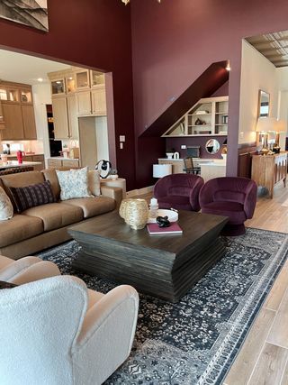 A cozy living room with rich maroon walls, modern furniture, and an elegant open plan leading to a chic kitchen.