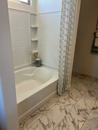 A sleek bathroom featuring a tiled bathtub, marble pattern flooring, and a stylish shower curtain.