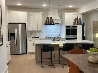 A modern kitchen with sleek white cabinetry, stainless steel appliances, and elegant pendant lighting.