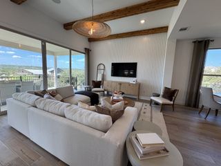 Model Home A bright living room with vaulted ceilings, exposed wood beams, a cozy white sofa, and panoramic views through large sliding glass doors.