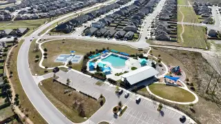 Community Amenities A vibrant community pool area in Crosswinds by Pulte Homes in Kyle, TX, featuring shaded lounge spaces, a splash pad, and a resort-style swimming pool.