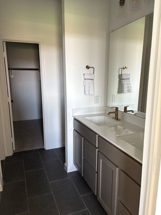 A sleek bathroom with a wide mirror, double sink vanity, modern fixtures, and dark tile flooring.