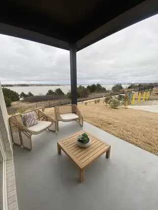 Model Home A cozy patio with woven chairs and a wooden table, offering a serene lake view under a cloudy sky.