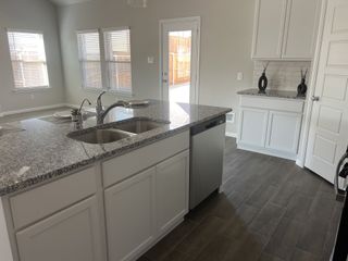A spacious kitchen with granite countertops, white cabinetry, and stainless steel appliances in Woodmere by M/I Homes (Denton, TX).