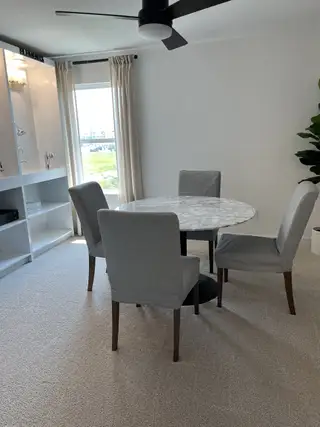 A cozy dining area with a round marble table, gray chairs, and large window, creating a bright and inviting space.