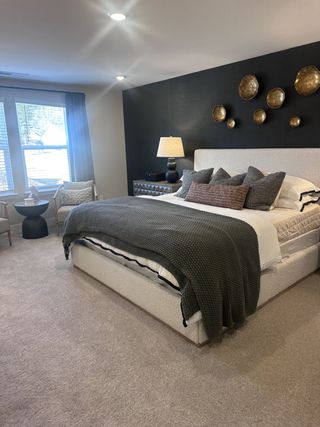 A cozy bedroom featuring a textured accent wall, large windows, and elegant decor with a plush carpet and modern lighting.