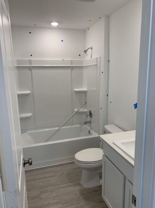 Model Home A cozy bathroom with a sleek white bathtub, light wood flooring, and compact vanity, offering a clean and modern look.